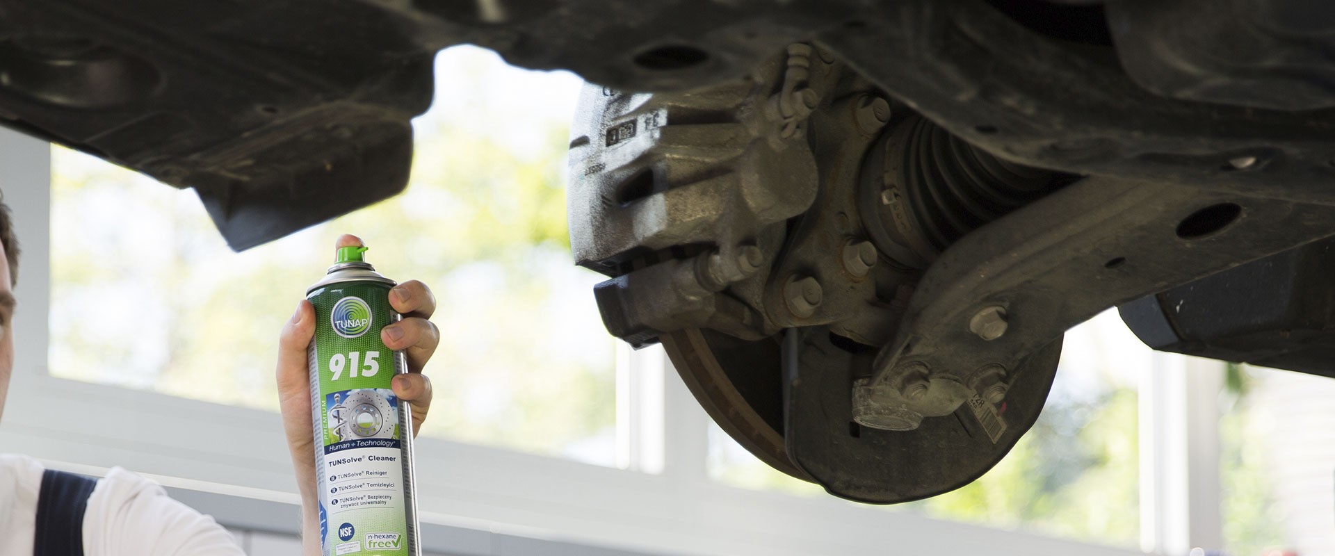 Person points a green spray can towards a dirty brake of a lifted car