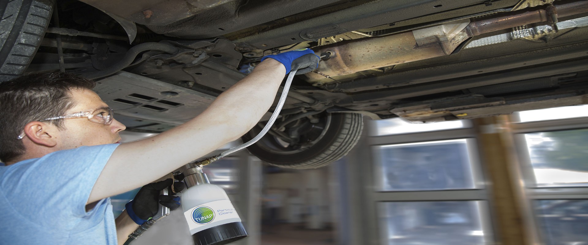 Mechanic under a lifted car using a cup gun with hose and probe to clean a diesel particulate filter