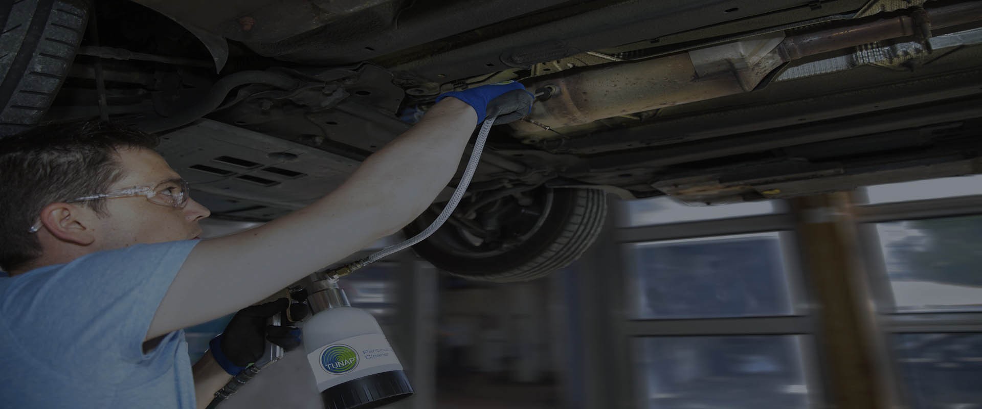 Mekaniker under en upplyft bil använder en koppspruta med slang och givare för att rengöra ett dieselpartikelfilter