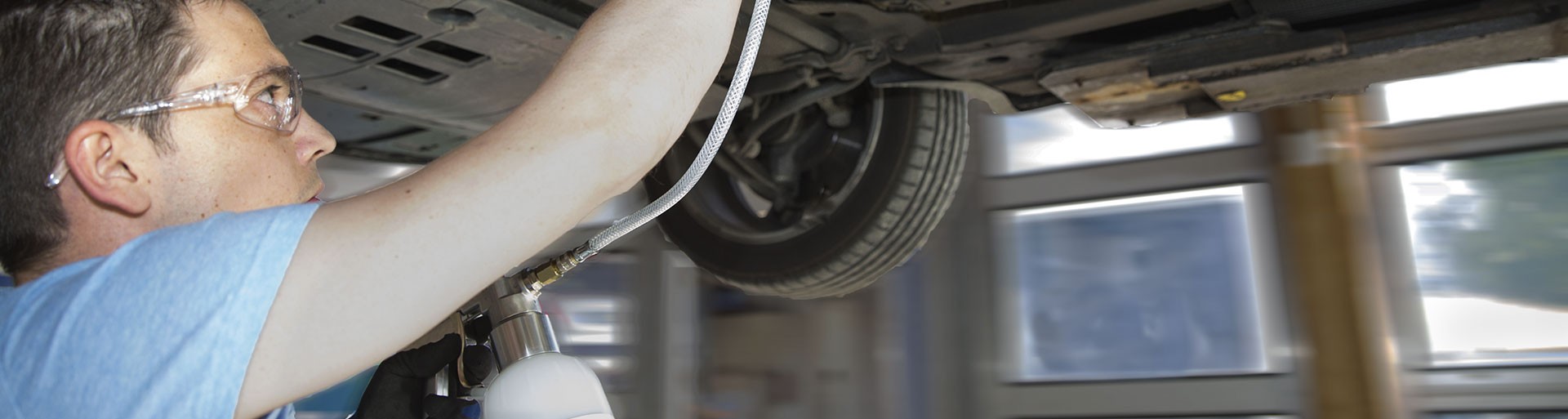 Mechanic under a lifted car using a cup gun with hose and probe to clean a diesel particulate filter