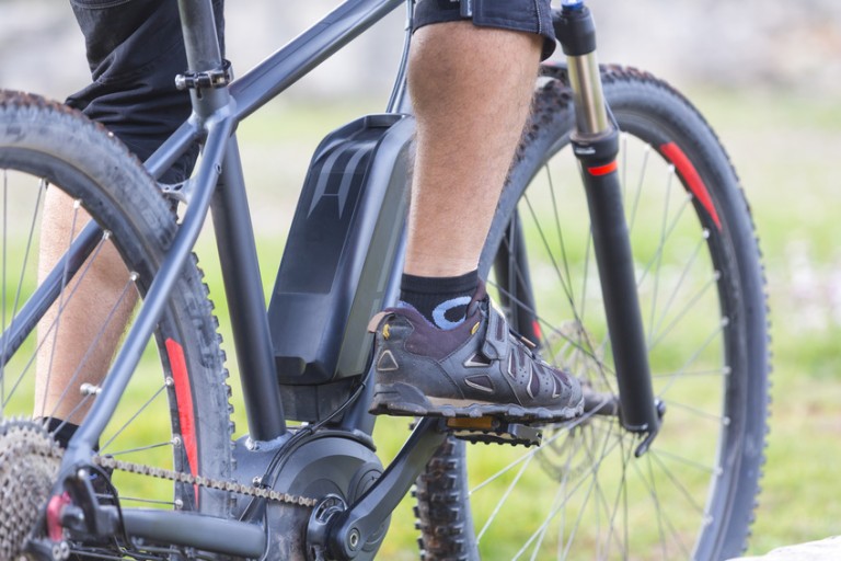 El-cykel Ben och gymnastikskor på pedalerna till en svart el-cykel
