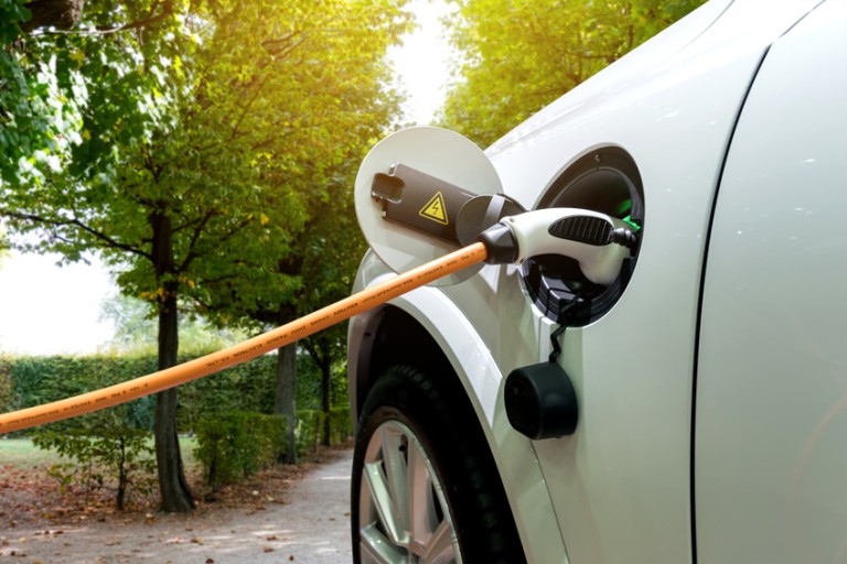 E-mobilitetslastning Orange laddningskabel instoppad i tanköppningen på en vit bil
