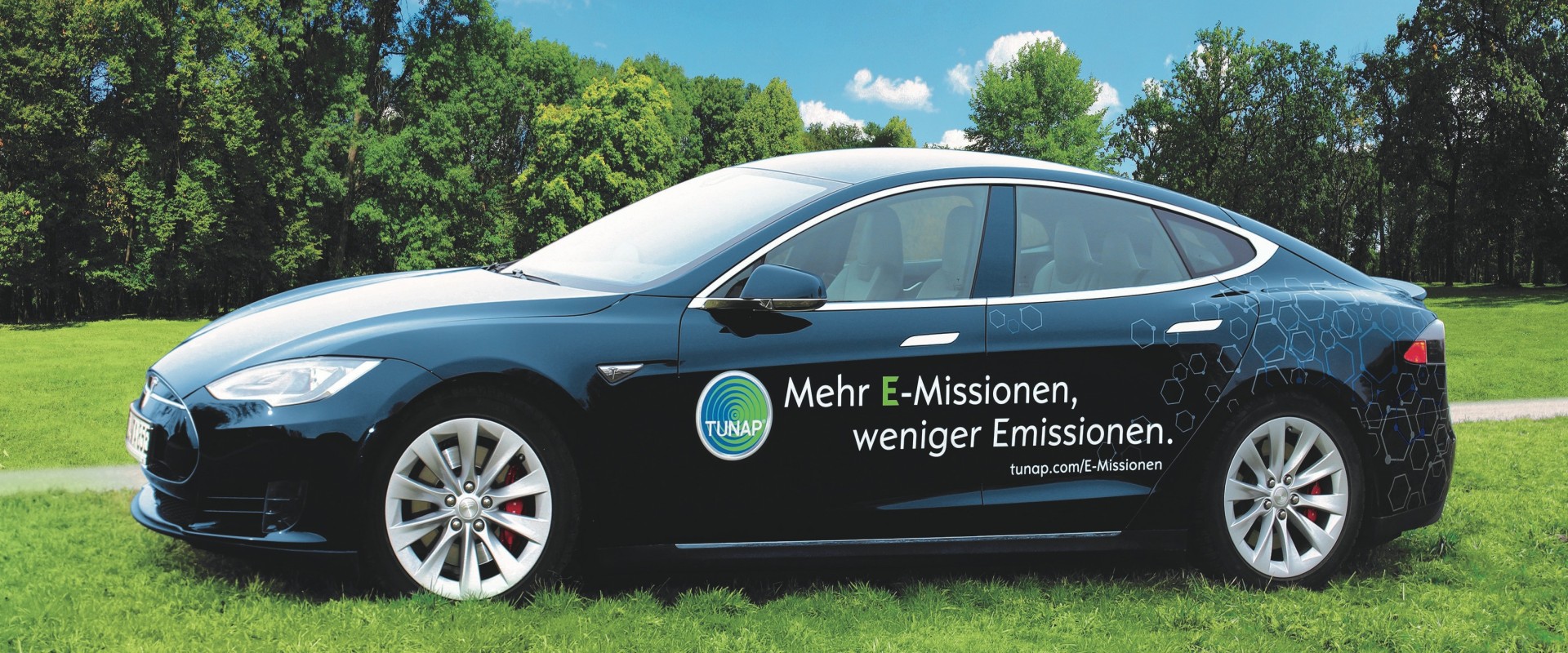 Side view of a dark blue sports car with white lettering and a TUNAP logo on a green meadow