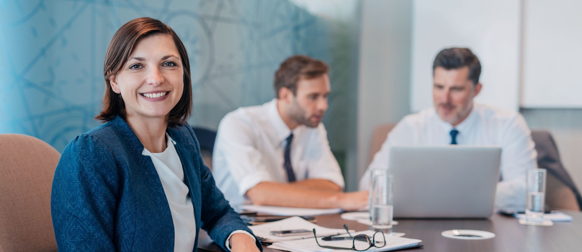 Portrait of a smiling young businesswoman sitting at a table with colleagues working in the background