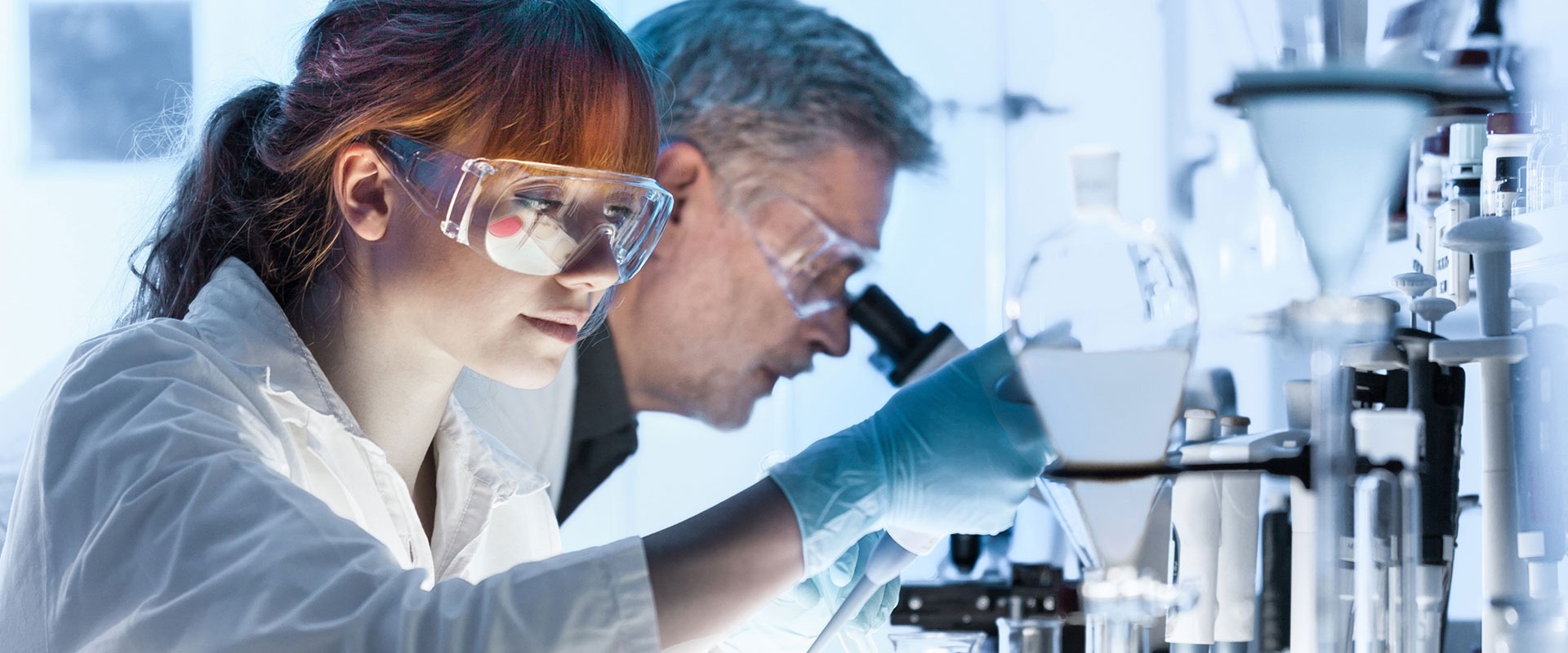 Smiling laboratory chemist wearing glasses and in the background a microscope and test tubes